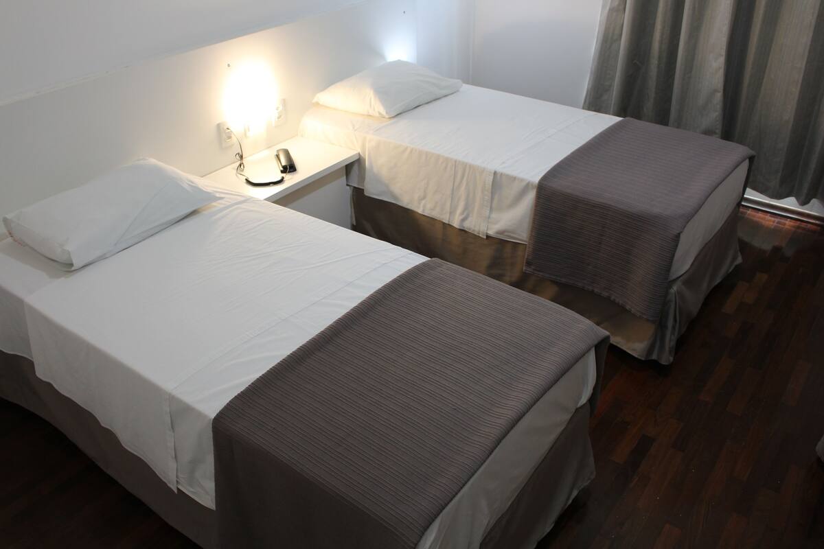 Two single beds with white linens and brown headboards in a hotel room.