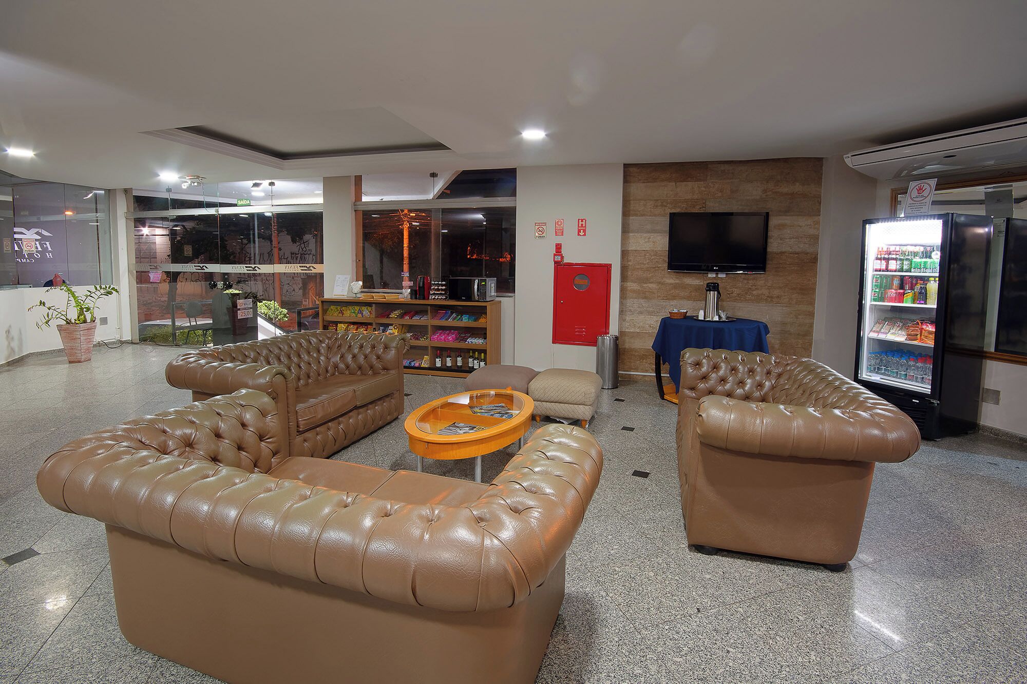 A lobby with leather sofas, a coffee table, a TV, and a refrigerator.