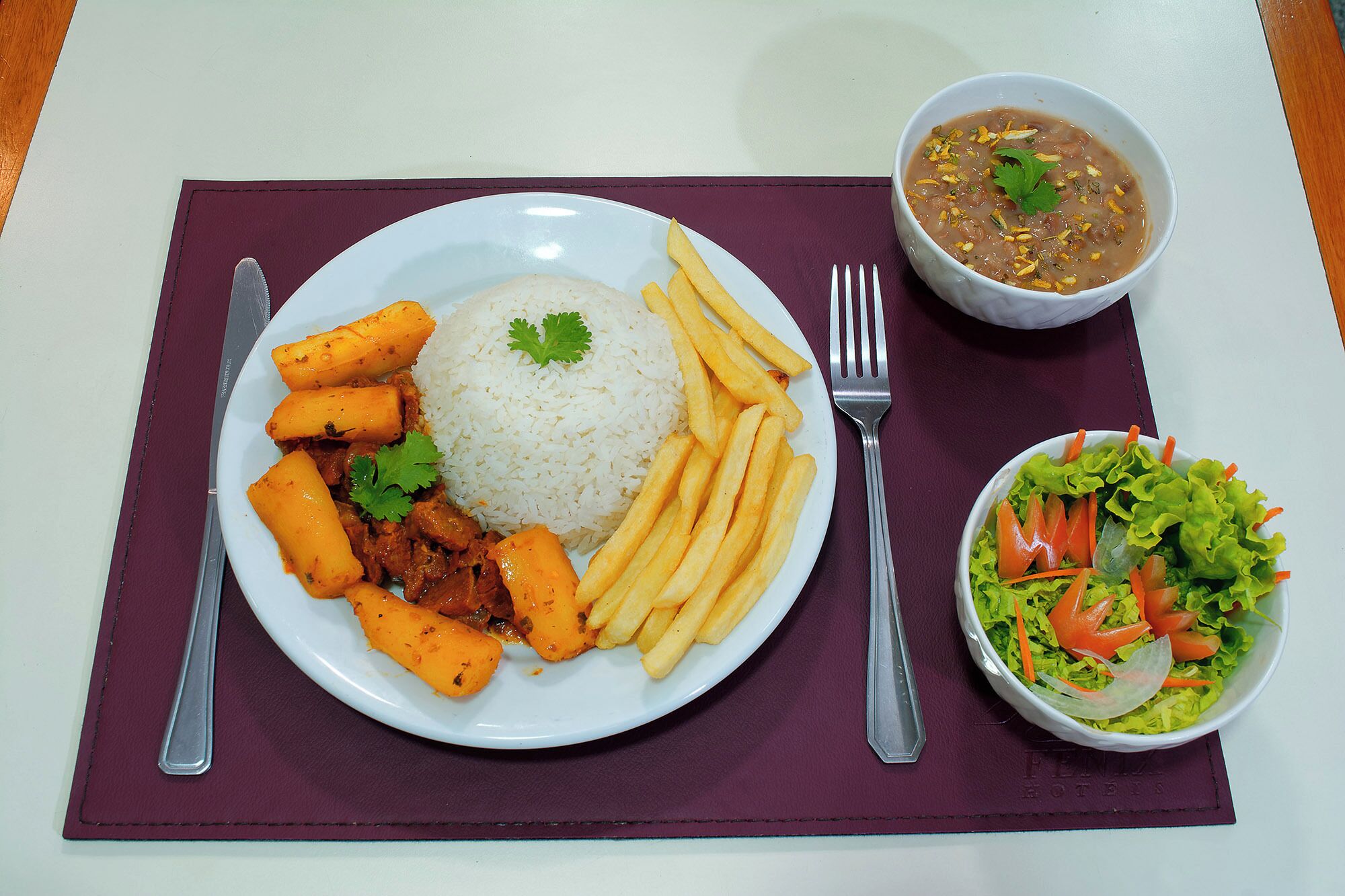 A plate with rice, meat, and fries, a bowl of soup, and a salad on a table with a placemat.