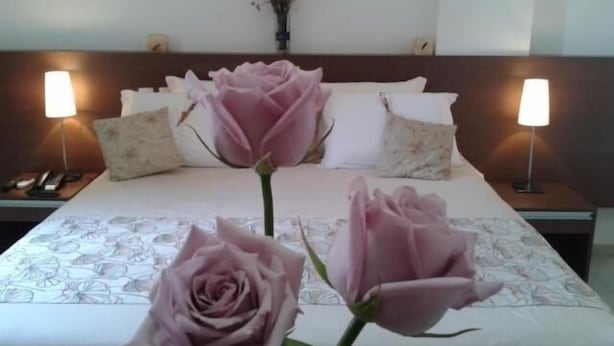 Habitación de hotel con una cama, dos lámparas de noche, un jarrón con flores y un teléfono en la mesita.