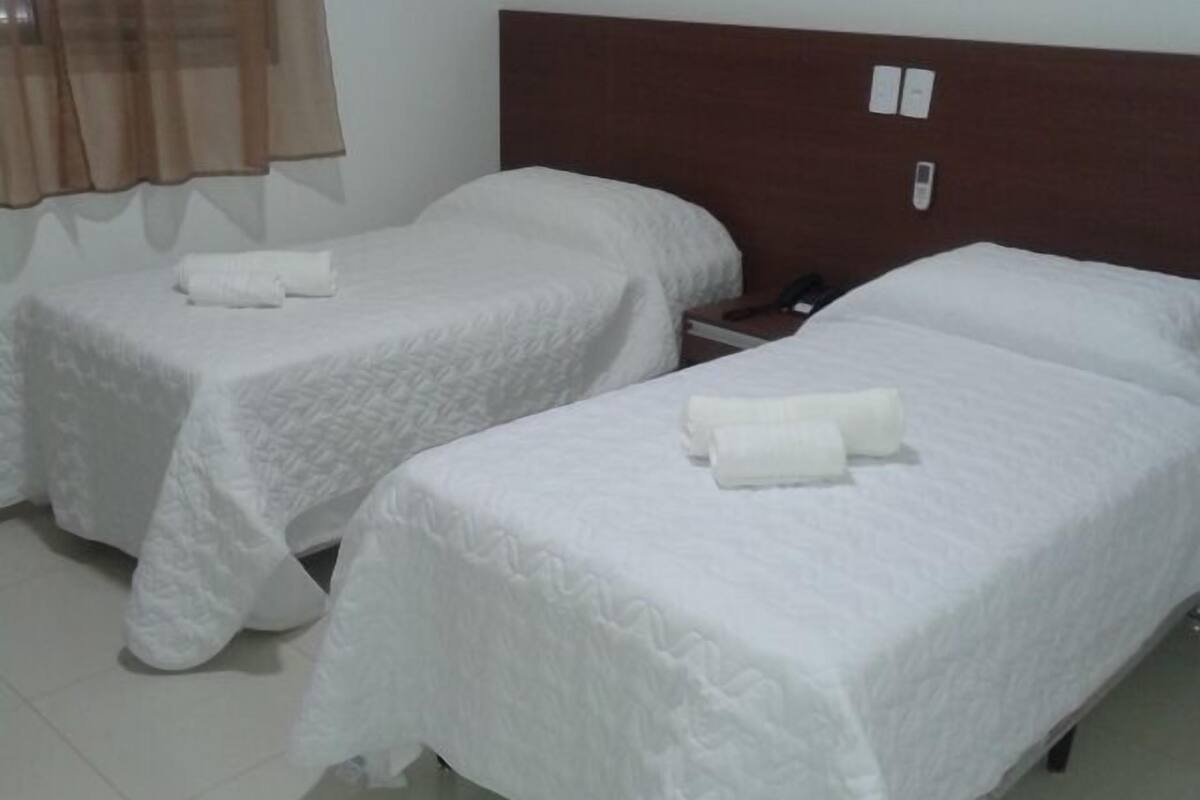 A hotel room with two single beds, each with a white bedspread and a rolled towel.