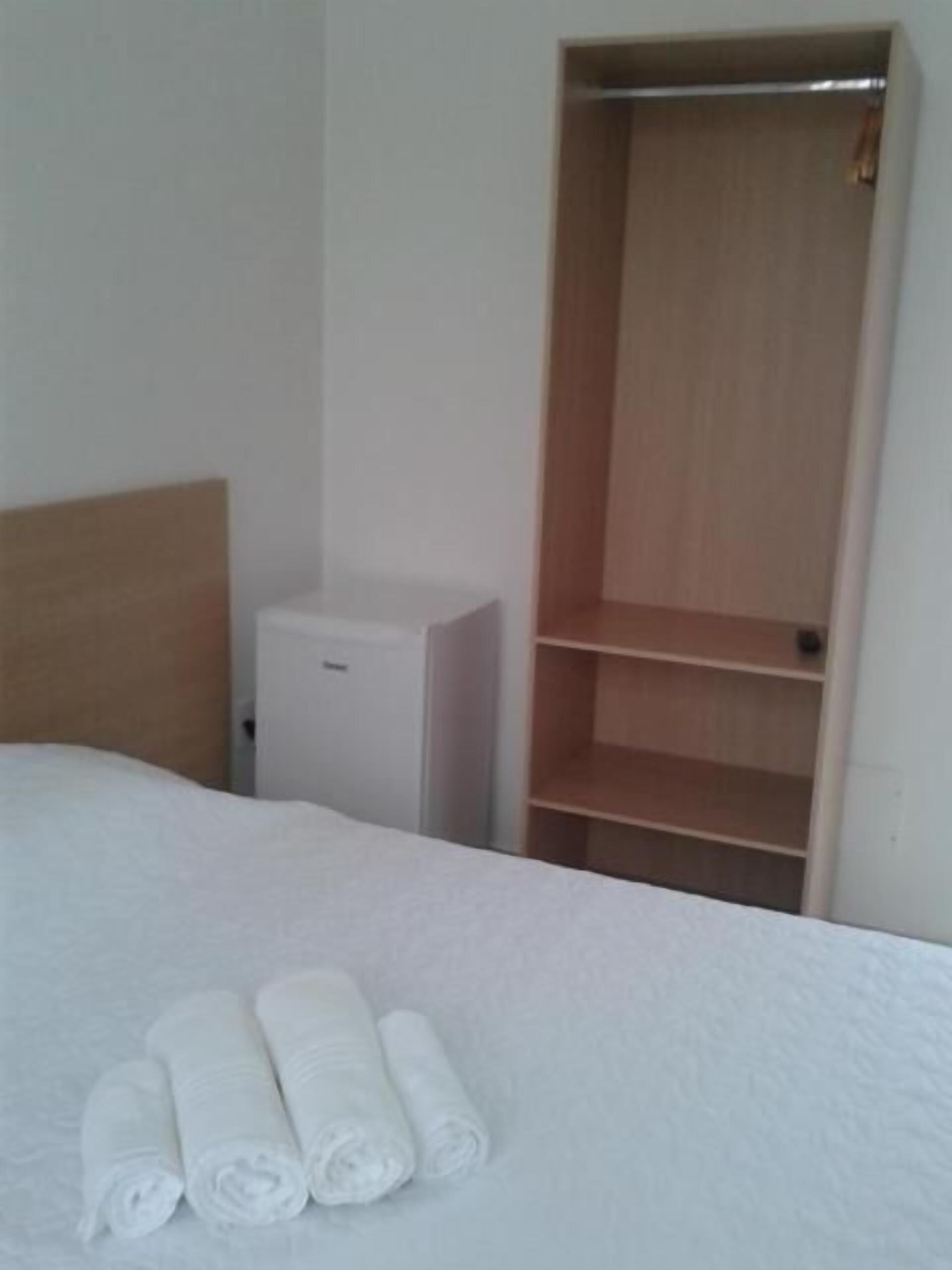 Una habitación de hotel con una cama, un armario y un pequeño mueble blanco.