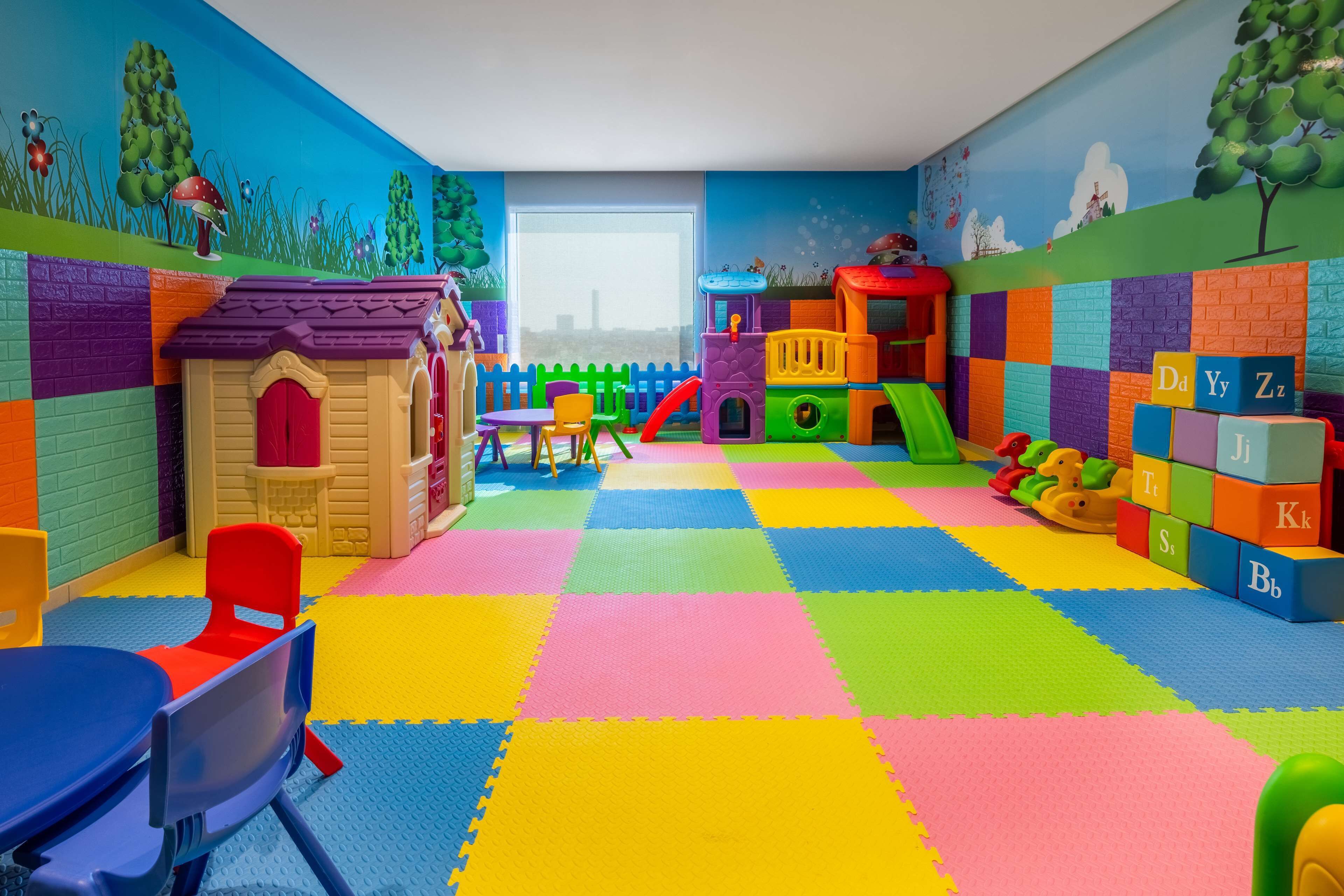 A playroom with colorful foam mats, a playhouse, a slide, and alphabet blocks.