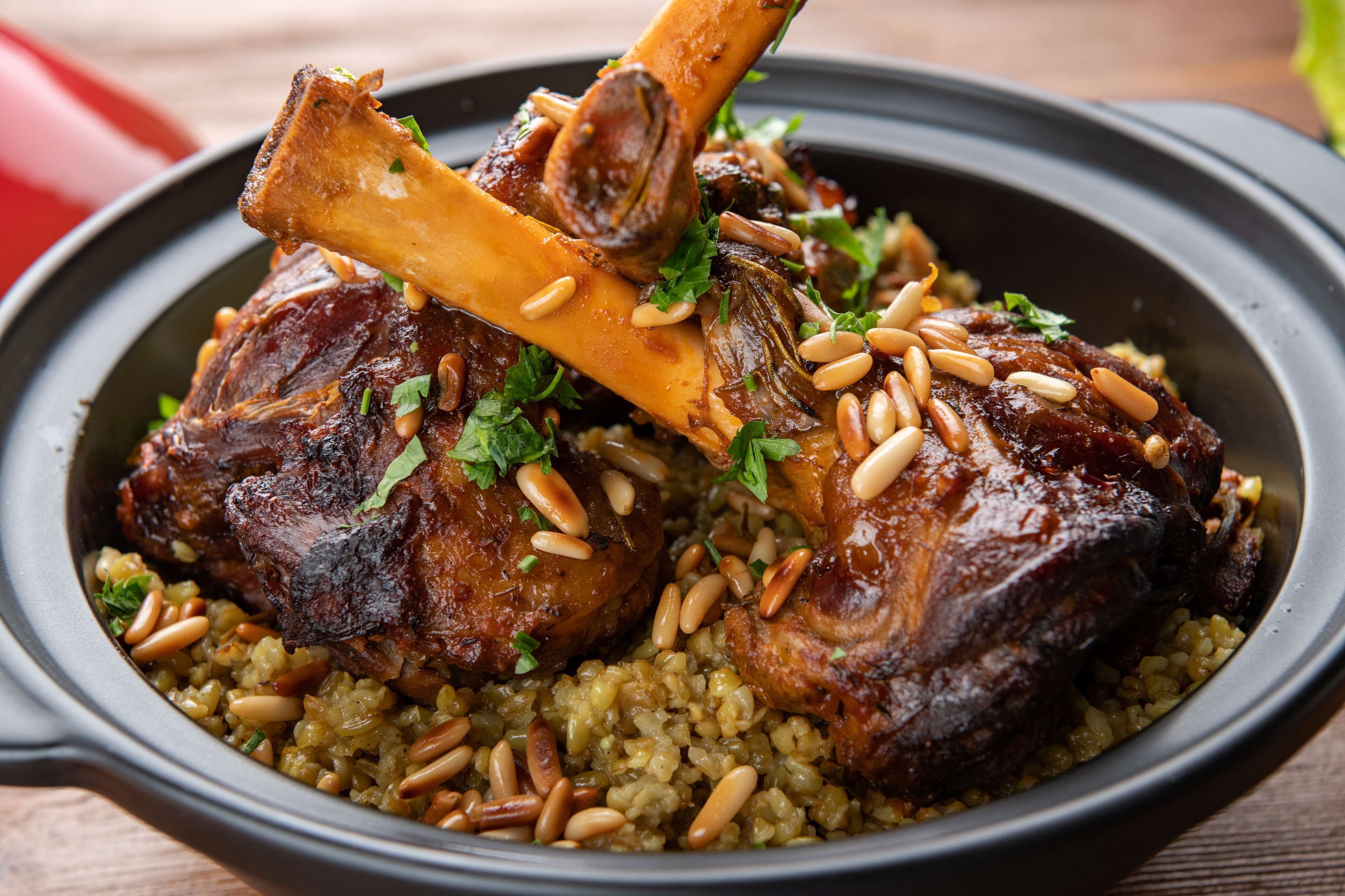 A dish with roasted meat and pine nuts on a bed of grains.