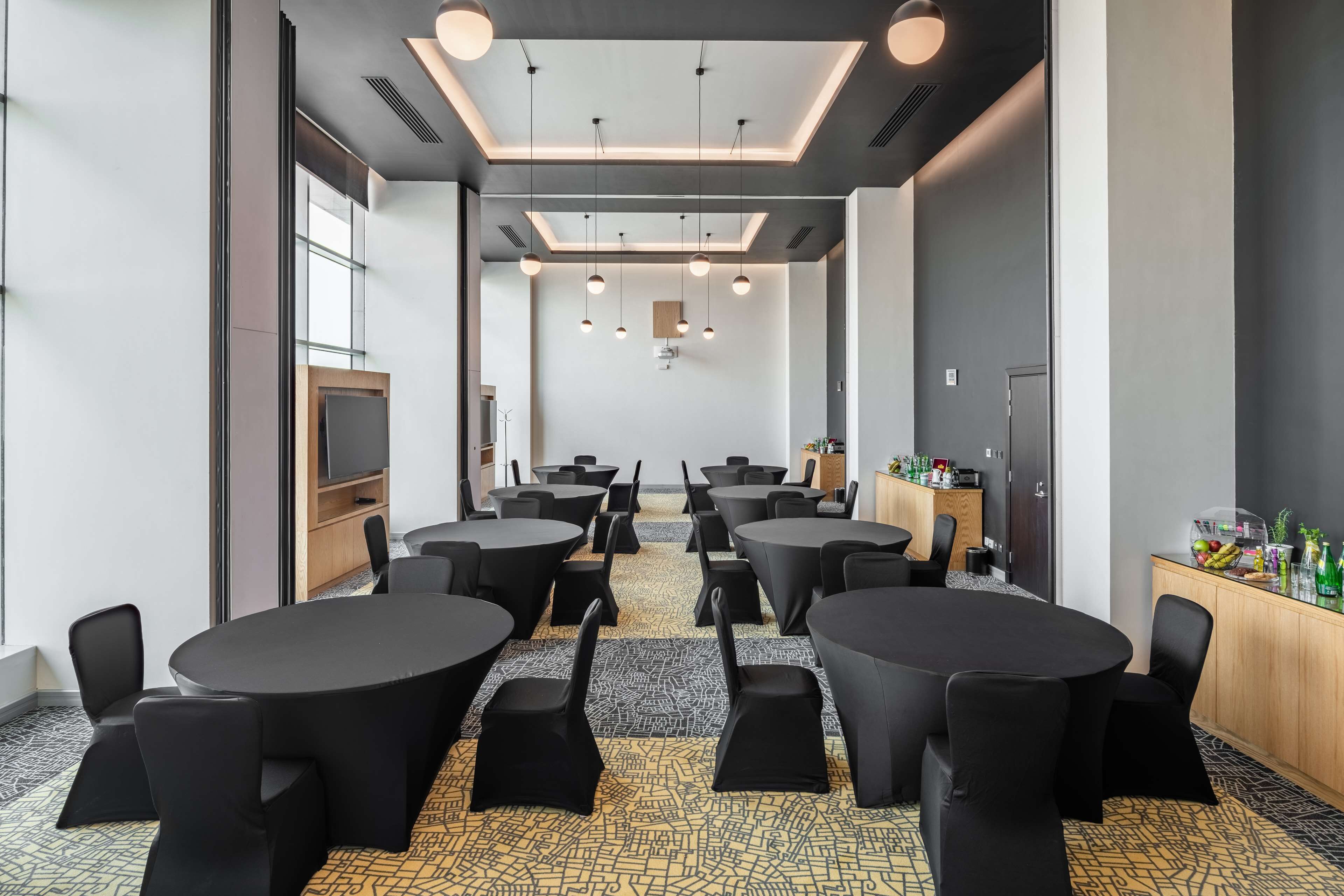 Une salle de conférence équipée de plusieurs tables rondes et de chaises, d’un téléviseur et d’un buffet proposant des collations.