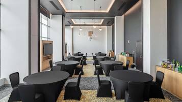 Une salle de conférence équipée de plusieurs tables rondes et de chaises, d’un téléviseur et d’un buffet proposant des collations.