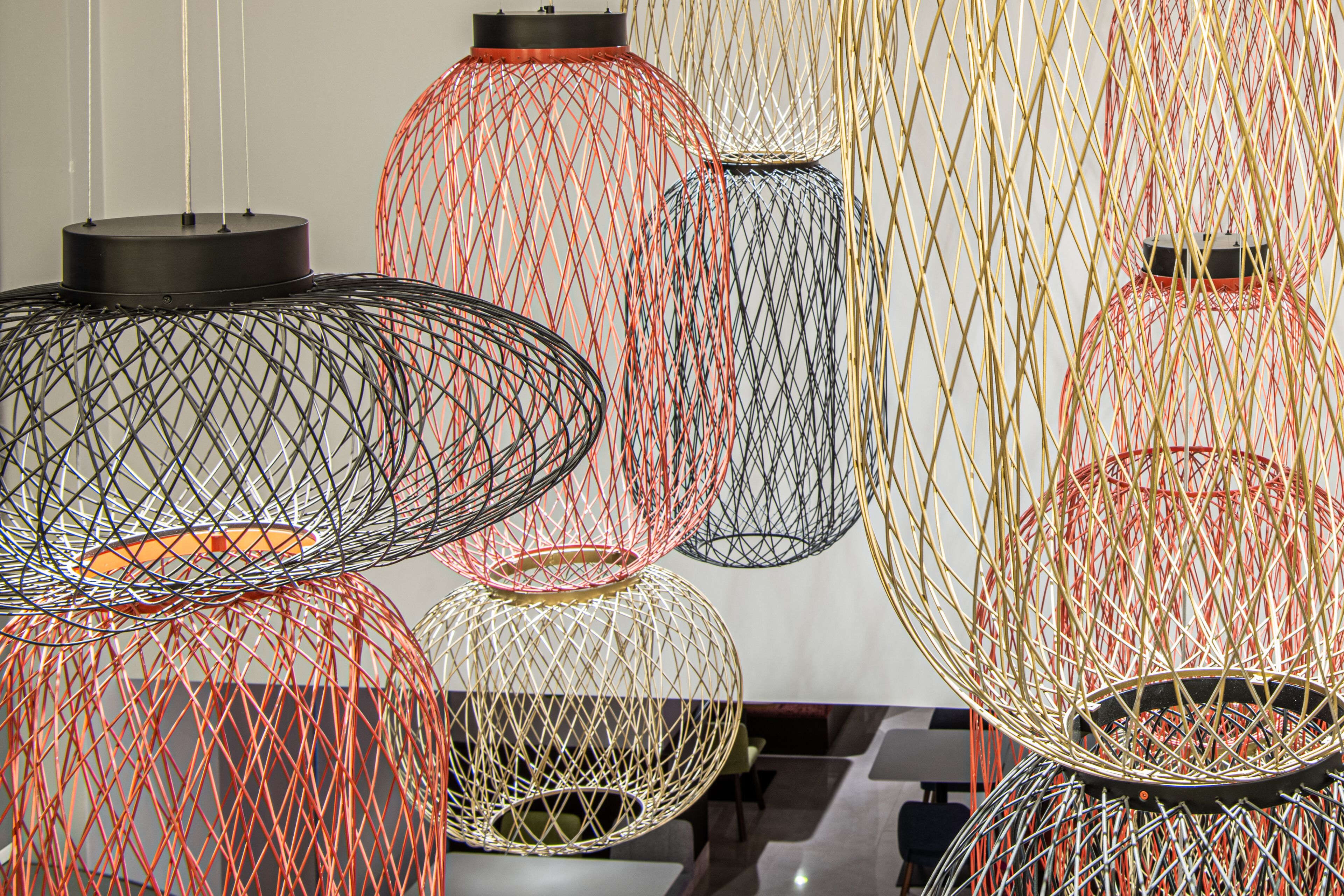 A series of spherical hanging light fixtures with a wireframe design, varying in color and size, suspended from the ceiling.