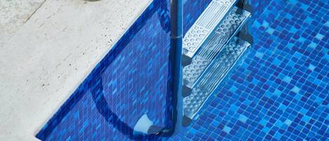 Parte de una piscina con mosaicos azules y una escalera de metal.