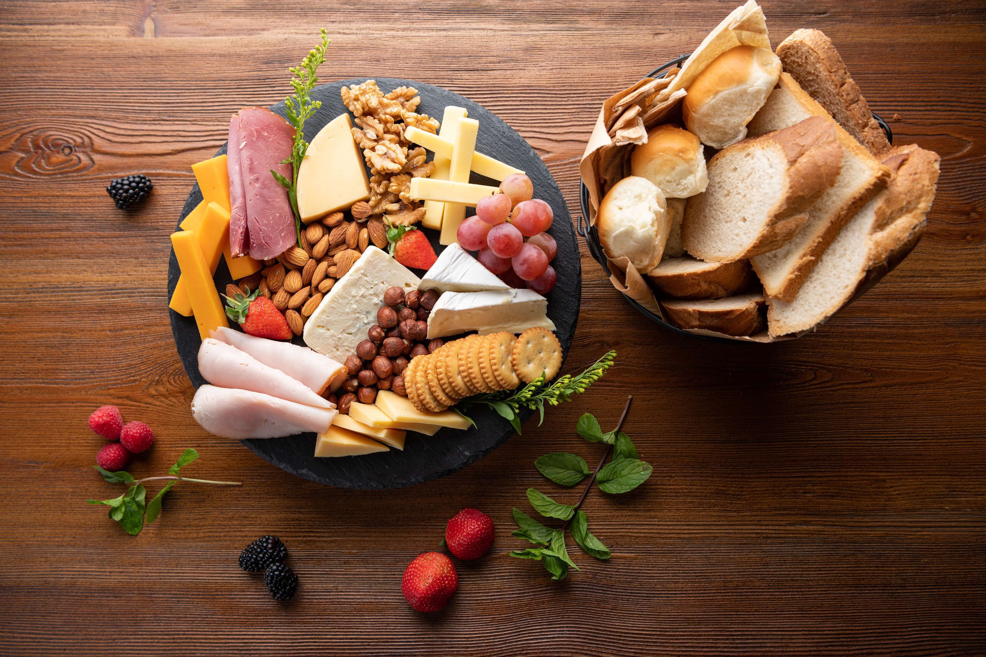 Una tabla de quesos y fiambres con frutos secos y frutas sobre una mesa de madera.