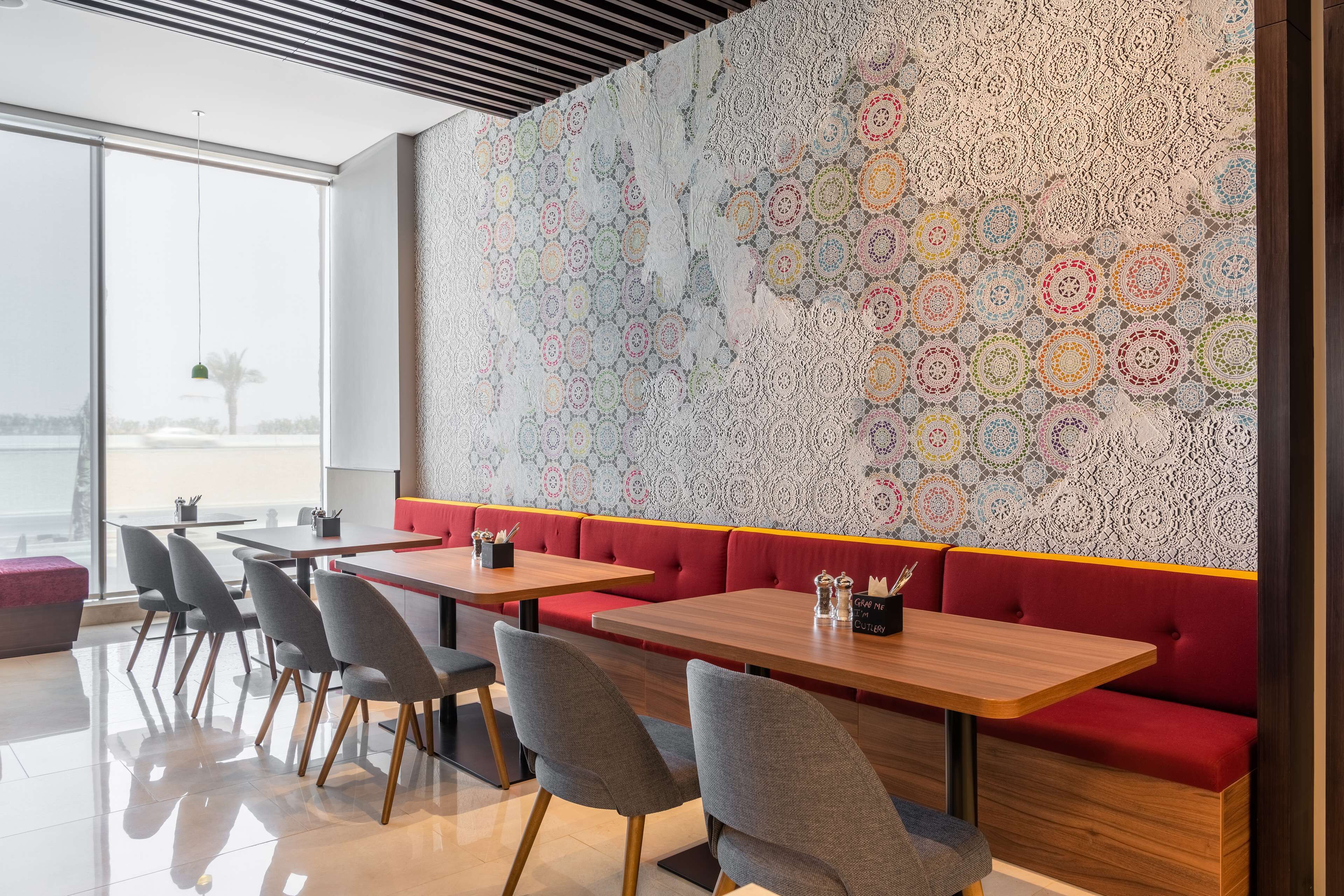 A modern restaurant with a patterned wall, wooden tables, and grey chairs.