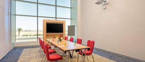 A conference room with a large table, red chairs, a large window, and a flat-screen TV.