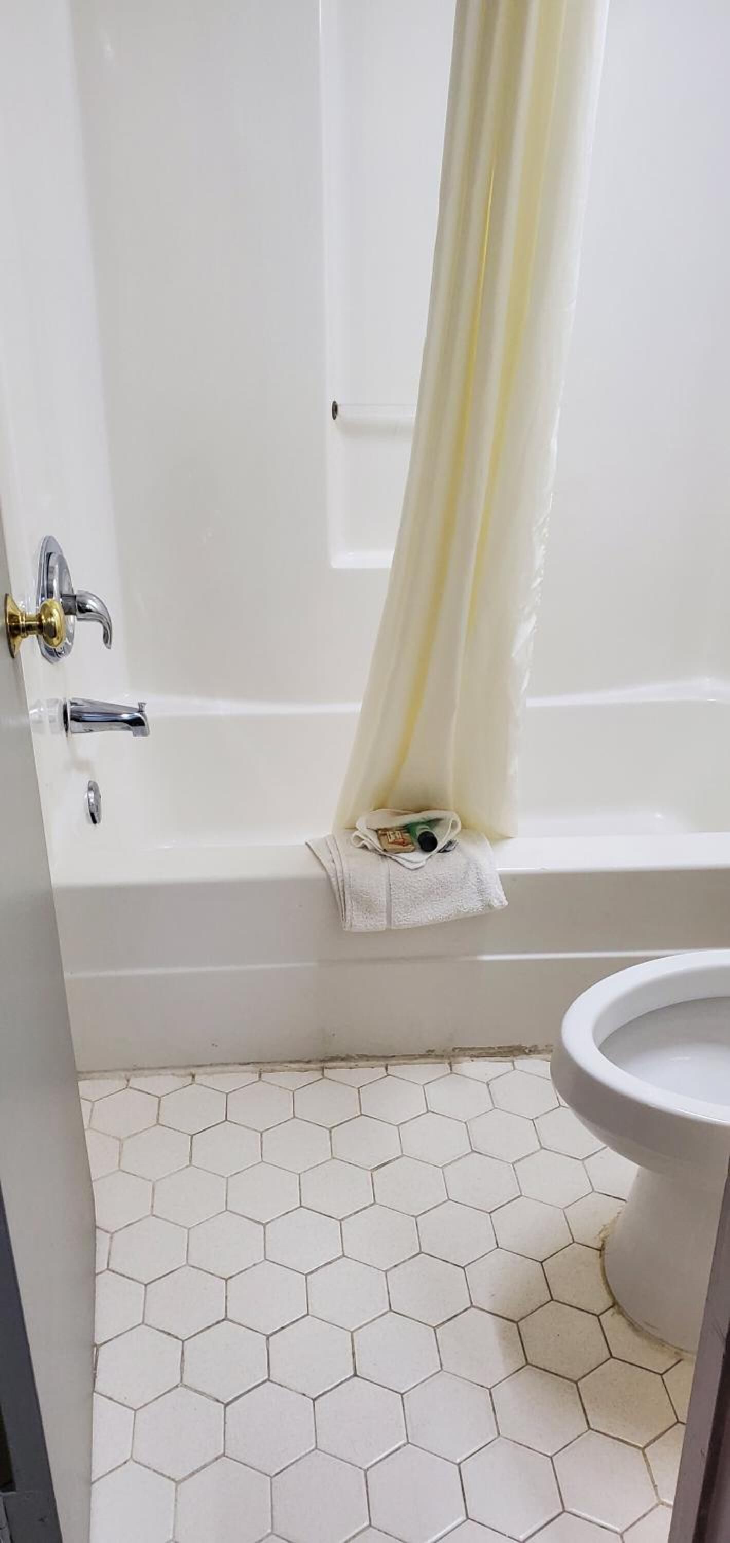 Un baño con una bañera blanca, un inodoro blanco y un suelo de baldosas hexagonales.