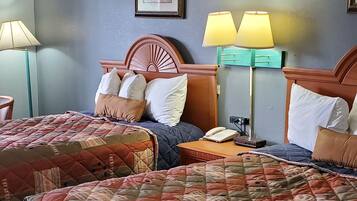 A hotel room with two beds, each with a quilted bedspread, a wooden headboard, and a bedside table with a lamp.