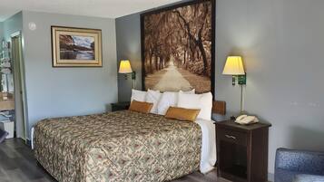 Habitación de hotel con una cama grande, dos lámparas de noche, una mesita de noche con un teléfono, un cuadro en la pared y una ventana con vistas a árboles.