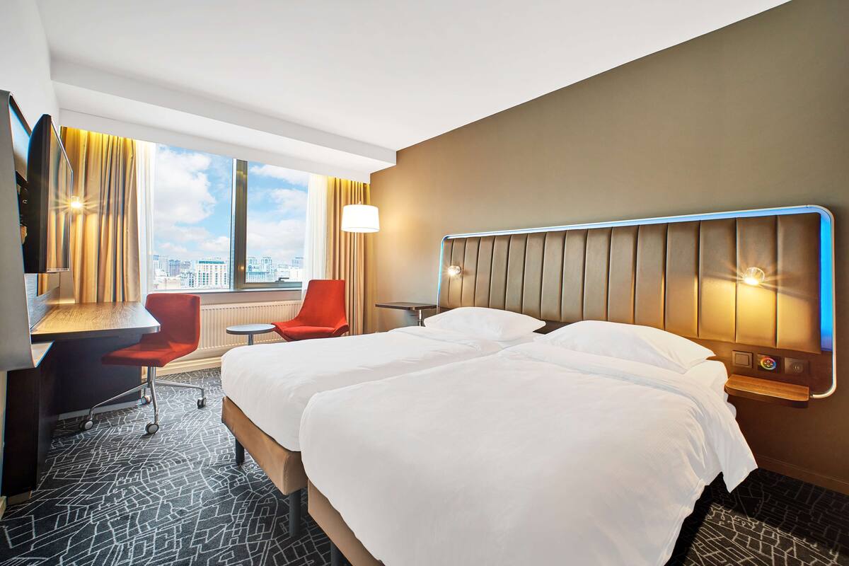 Ein Hotelzimmer mit einem großen Bett, einem Schreibtisch, einem Stuhl und Blick auf die Stadt.