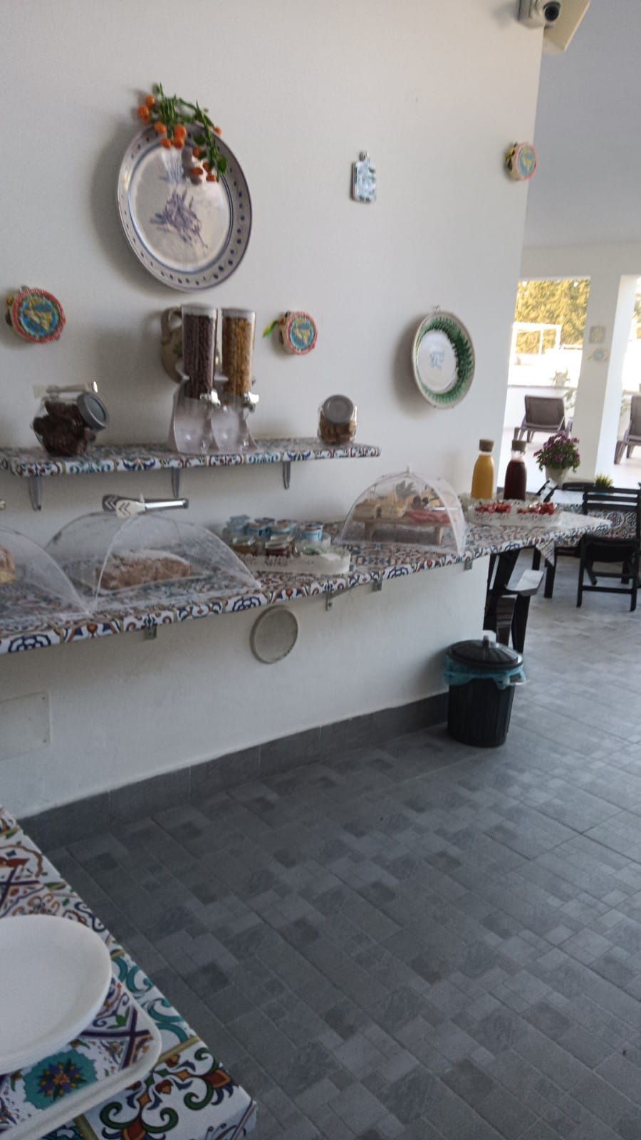 A kitchen area with a long countertop, various kitchenware, and a trash bin.