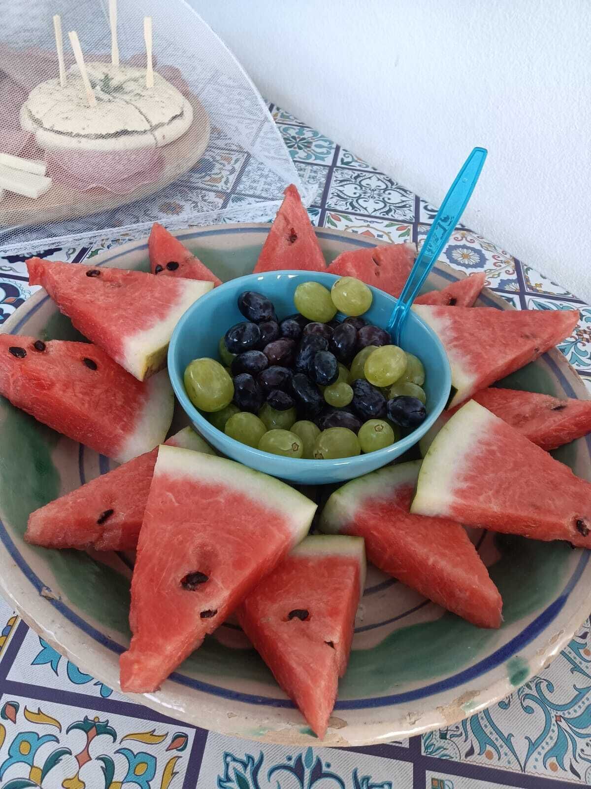 Un plato con rebanadas de sandía dispuestas en forma de estrella, alrededor de un bol de uvas y arándanos.
