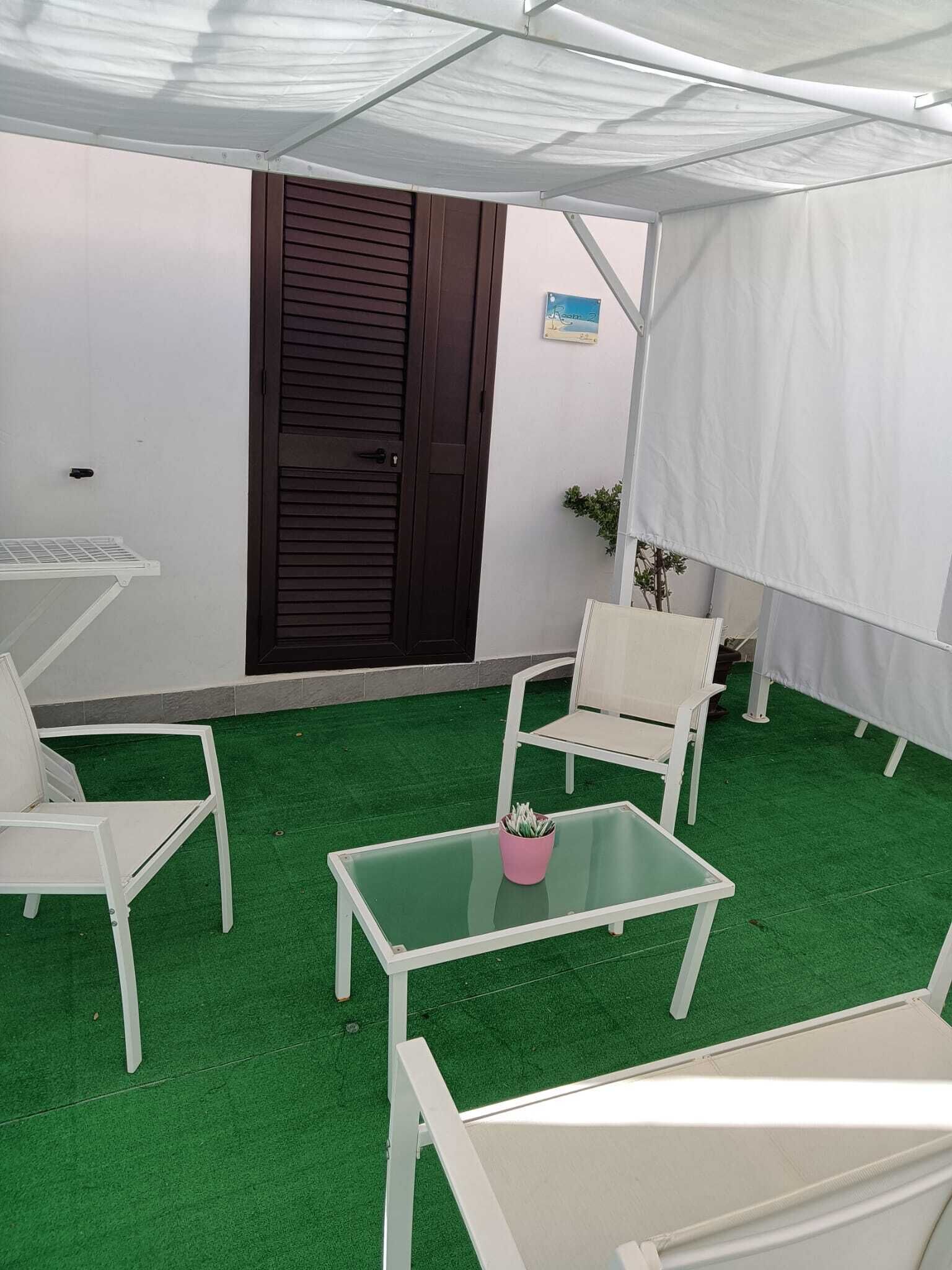 Een overdekt terras met witte meubels en kunstgras.