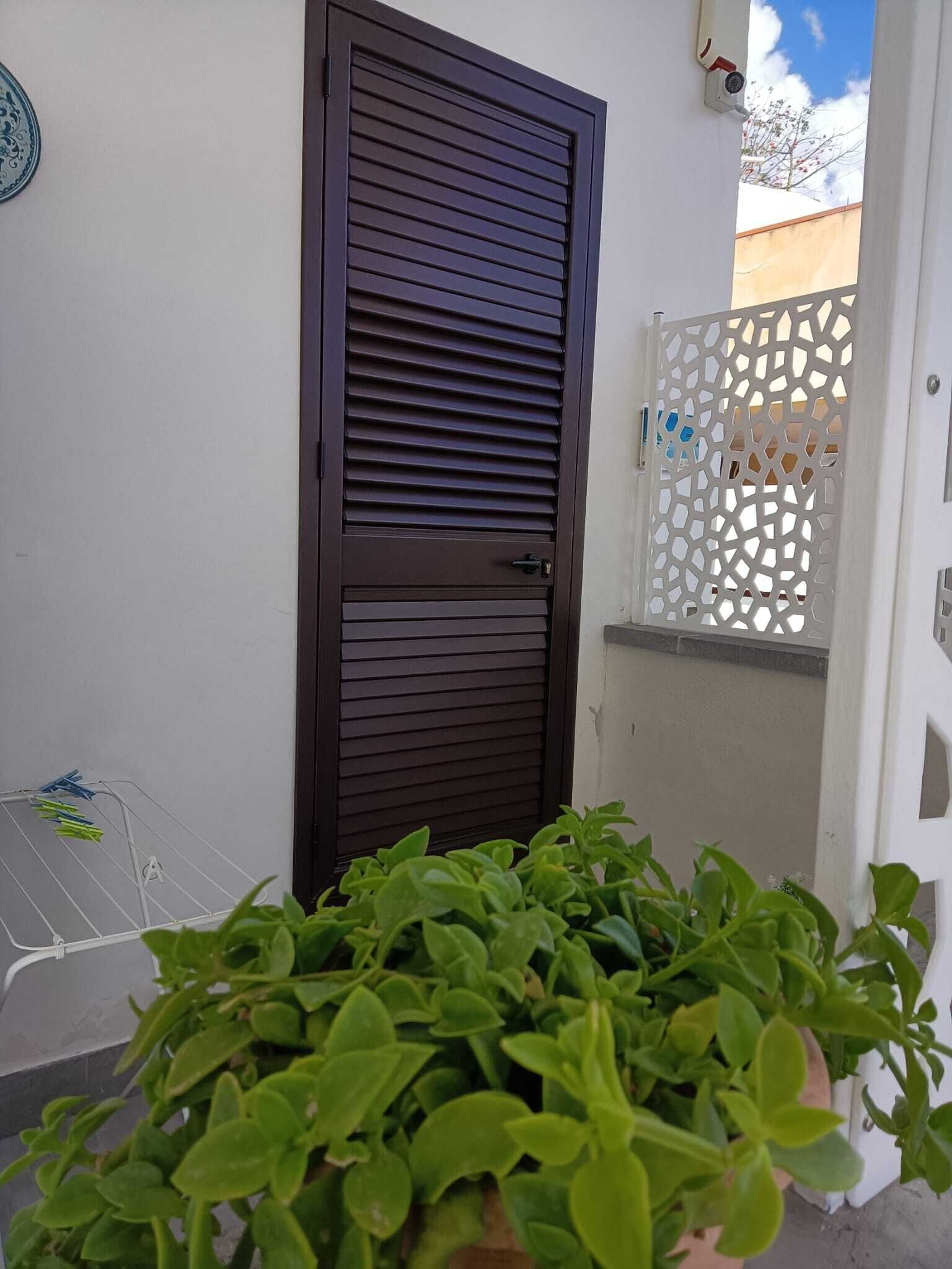 A dark brown door with horizontal slats, a white wall, and a white decorative fence.