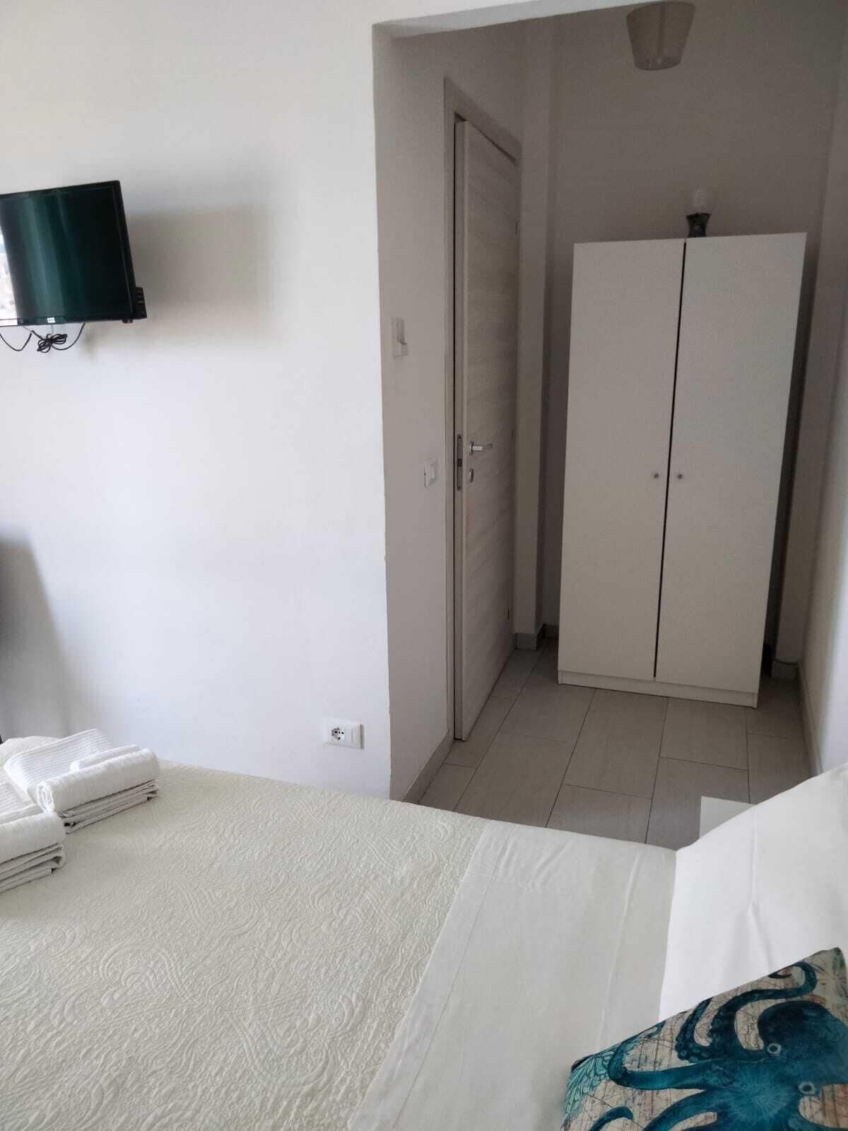 A hotel room with a bed, a TV mounted on the wall, a wardrobe, and a door leading to another room.
