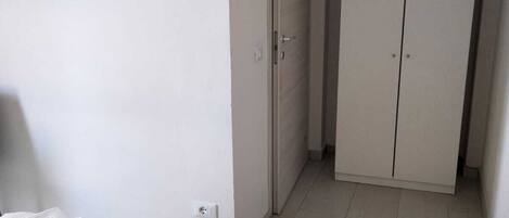 A hotel room with a bed, a TV mounted on the wall, a wardrobe, and a door leading to another room.