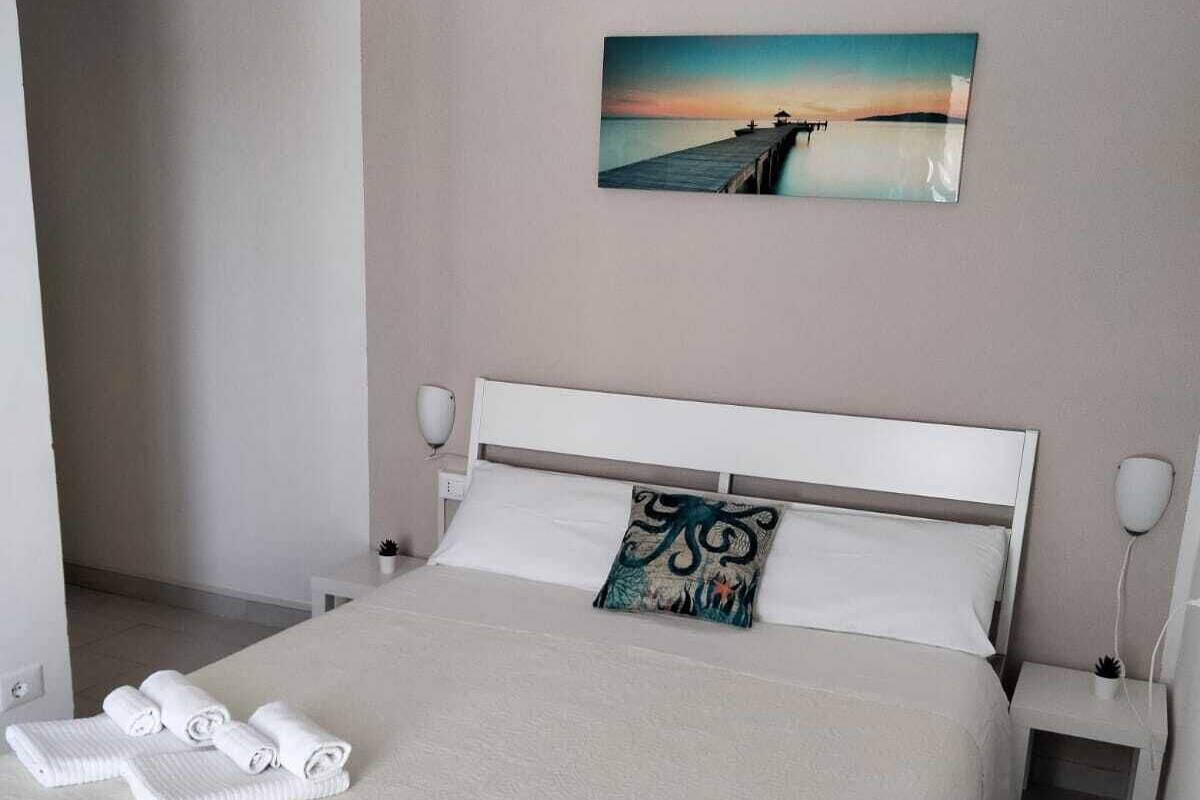 Ein ordentlich bezogenes Bett mit weißem Kopfteil, einem Kissen mit Blumenmuster und aufgerollten Handtüchern an der Seite.