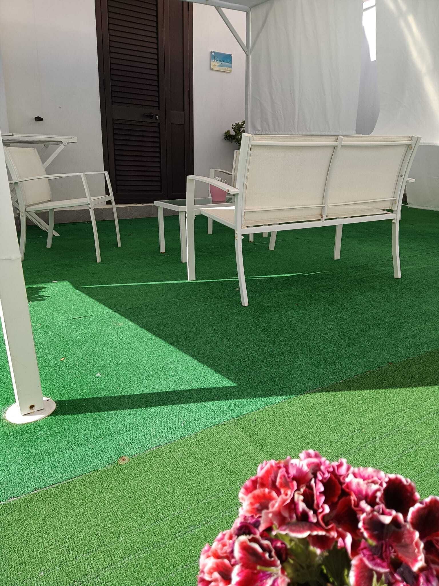 A patio area with artificial green turf, white metal chairs, and a white table.