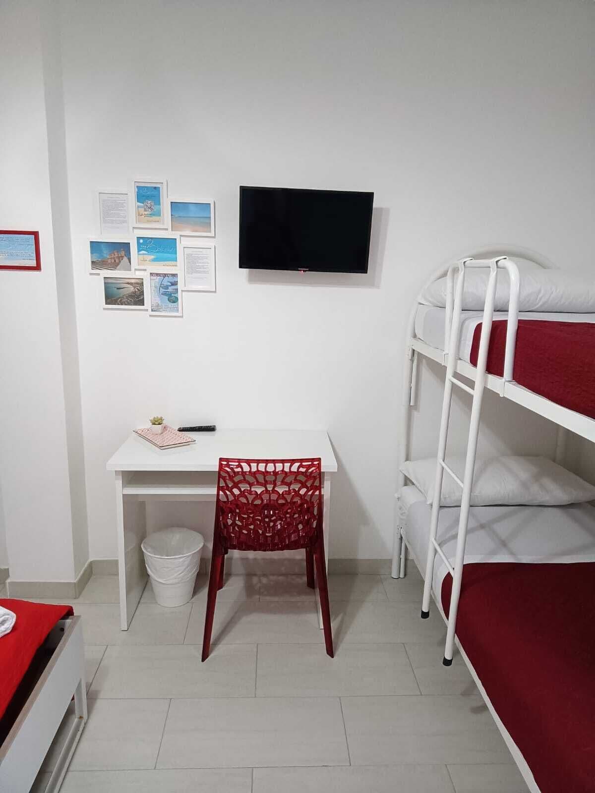 Una camera del dormitorio con un letto a castello, una scrivania, una sedia, una TV e una parete con poster informativi.