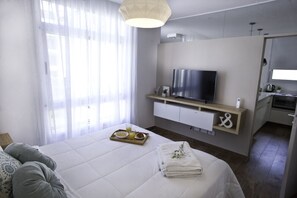 Ett modernt hotellrum med en säng, en TV, ett litet pentry och ett badrum.