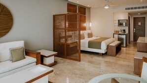 Una habitación de hotel moderna con cama, sofá, mesita de centro, mesa de comedor y kitchenette.