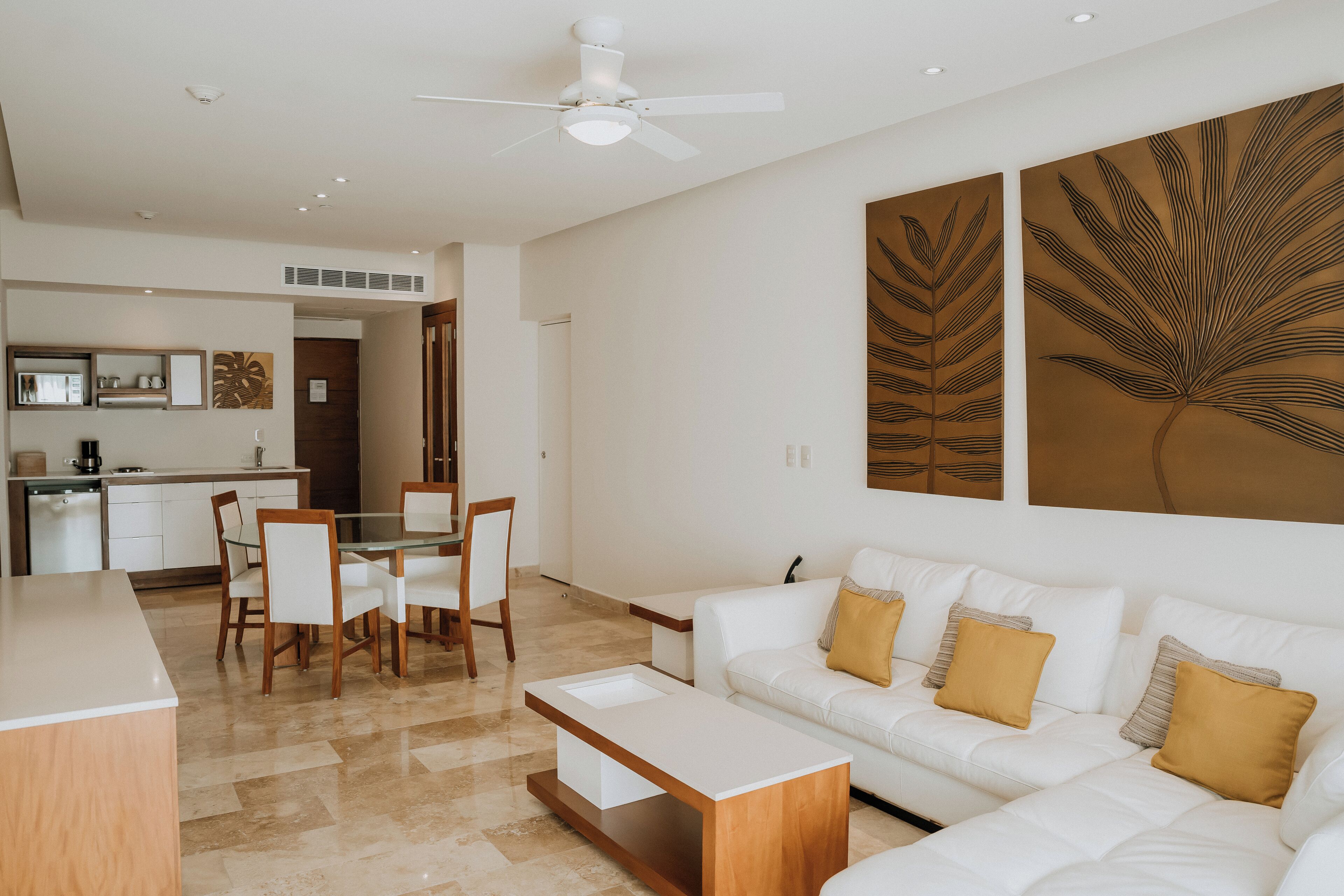 A modern living room with a white sofa, a glass coffee table, and a dining area with a white table and chairs.