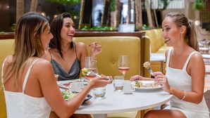 Un grupo de personas cenando en una mesa redonda en un restaurante, con un banco acolchado amarillo y una jarra de vidrio sobre la mesa.