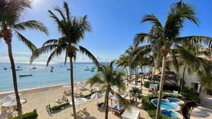 Una playa con palmeras, una piscina y varias embarcaciones en el agua.