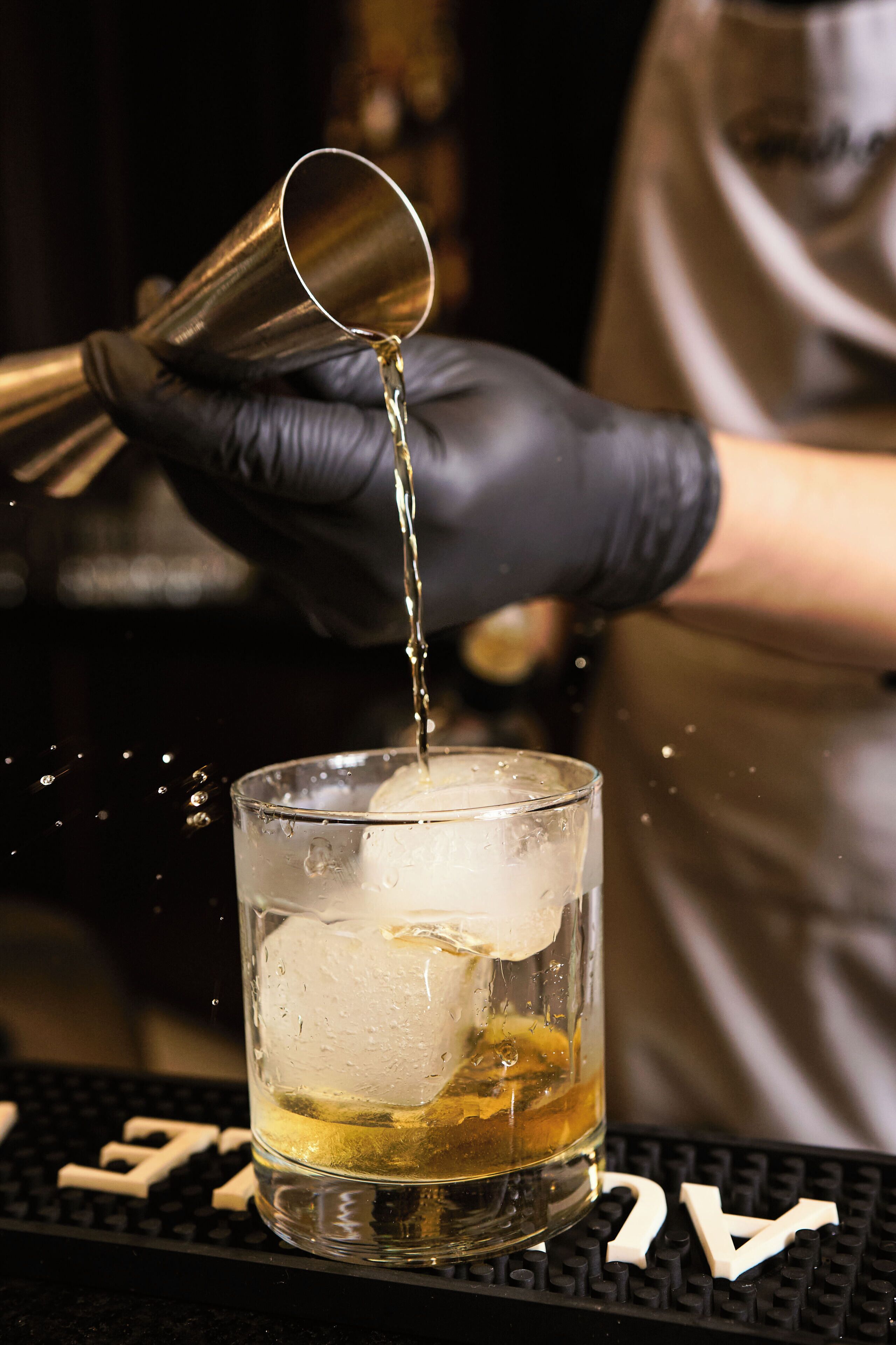 A person pouring a liquid into a glass with ice cubes.