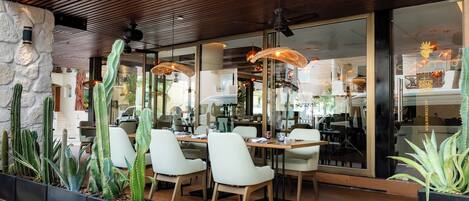 A restaurant with a wooden ceiling, cactus plants, and white chairs.