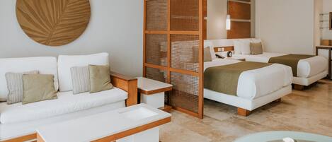 Una habitación de hotel moderna con un sofá blanco, una mesa de centro de madera, una cama con manta verde y un gran adorno mural.