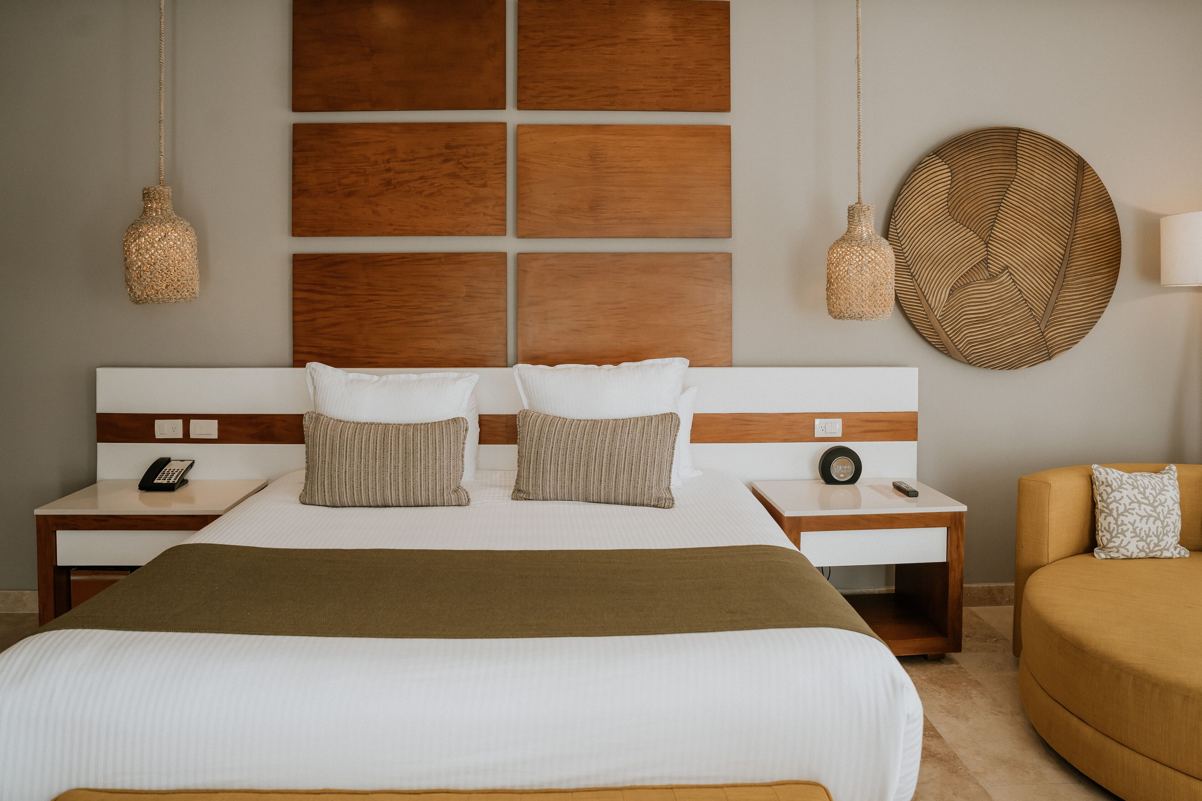 A hotel room with a large bed, two bedside tables with lamps, a wooden headboard, and a round woven wall decoration.
