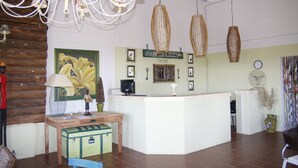 A reception area with a wooden desk, a green suitcase, and a painting of lilies. - Los Origenes (Concordia)