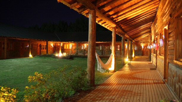A wooden building with a covered patio area, a hammock, and a well-lit interior. - Los Origenes (Concordia)
