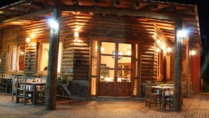 A log cabin with a wooden deck, outdoor seating, and a large glass door entrance. - Los Origenes (Concordia)