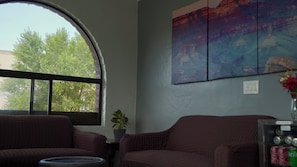 Una habitación con un amplio ventanal de arco, un sofá, una pequeña mesa con una planta y una obra de arte colgada en la pared.
