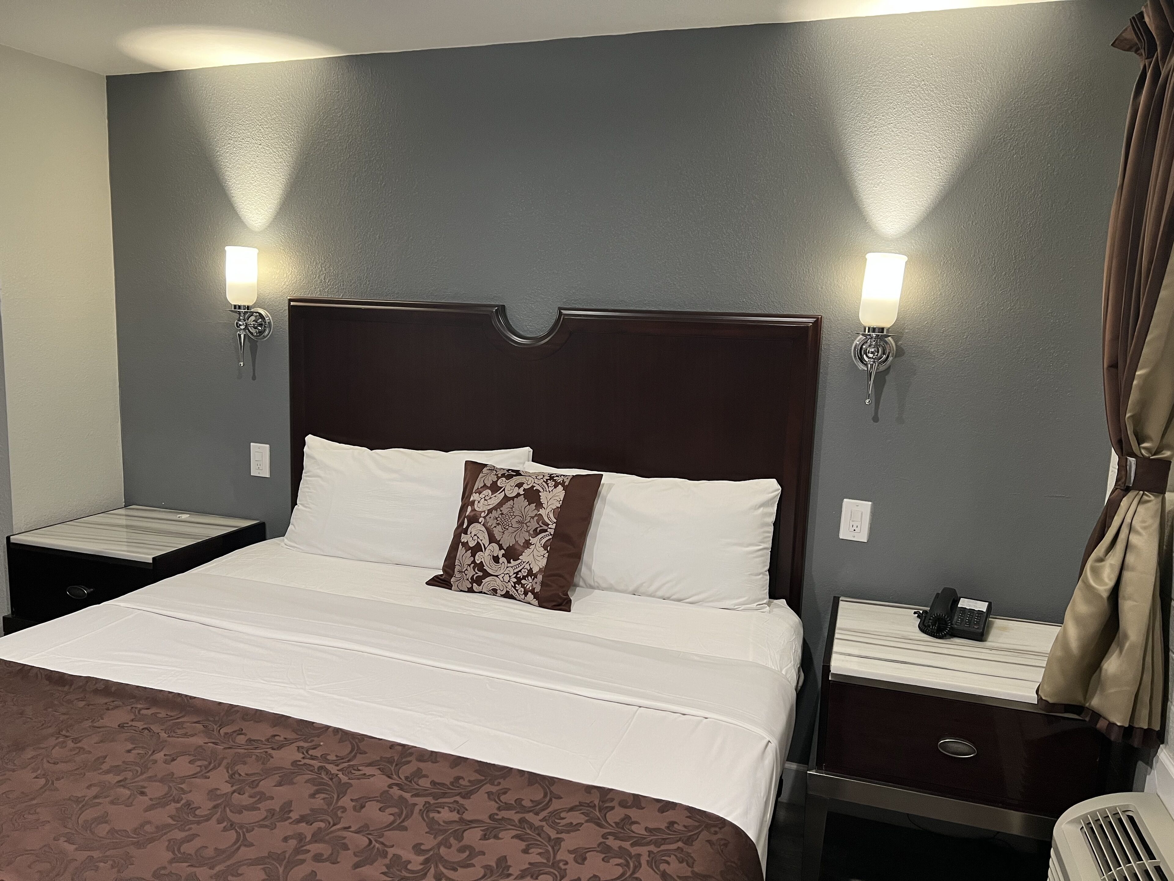 Una habitación de hotel con una cama grande, dos mesitas de noche, un teléfono y una lámpara a cada lado.