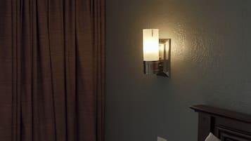 Una camera d'albergo con un letto, un comodino, una lampada a parete e una finestra con tende.