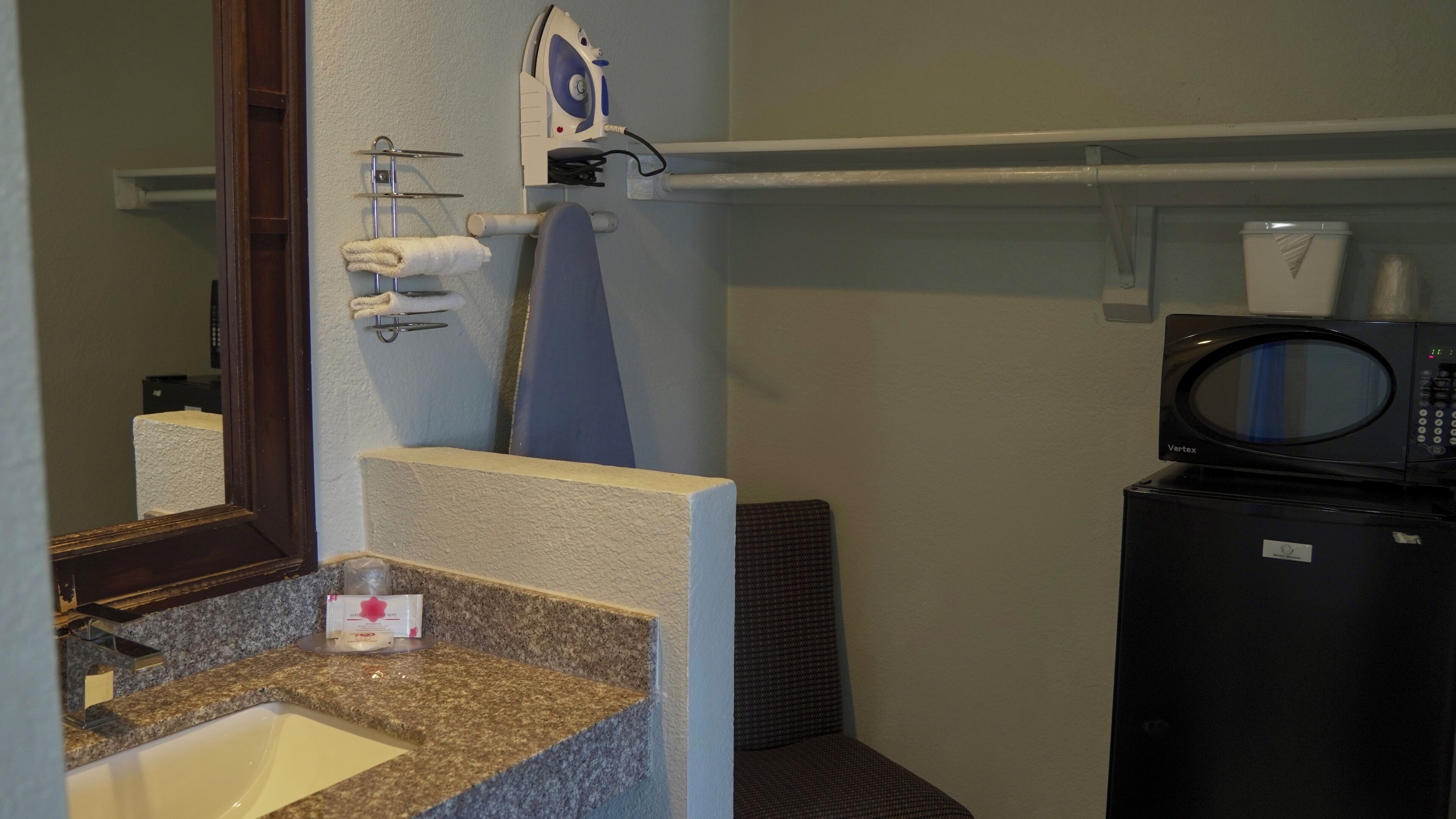 A bathroom with a sink, mirror, towel rack, iron, and a microwave.