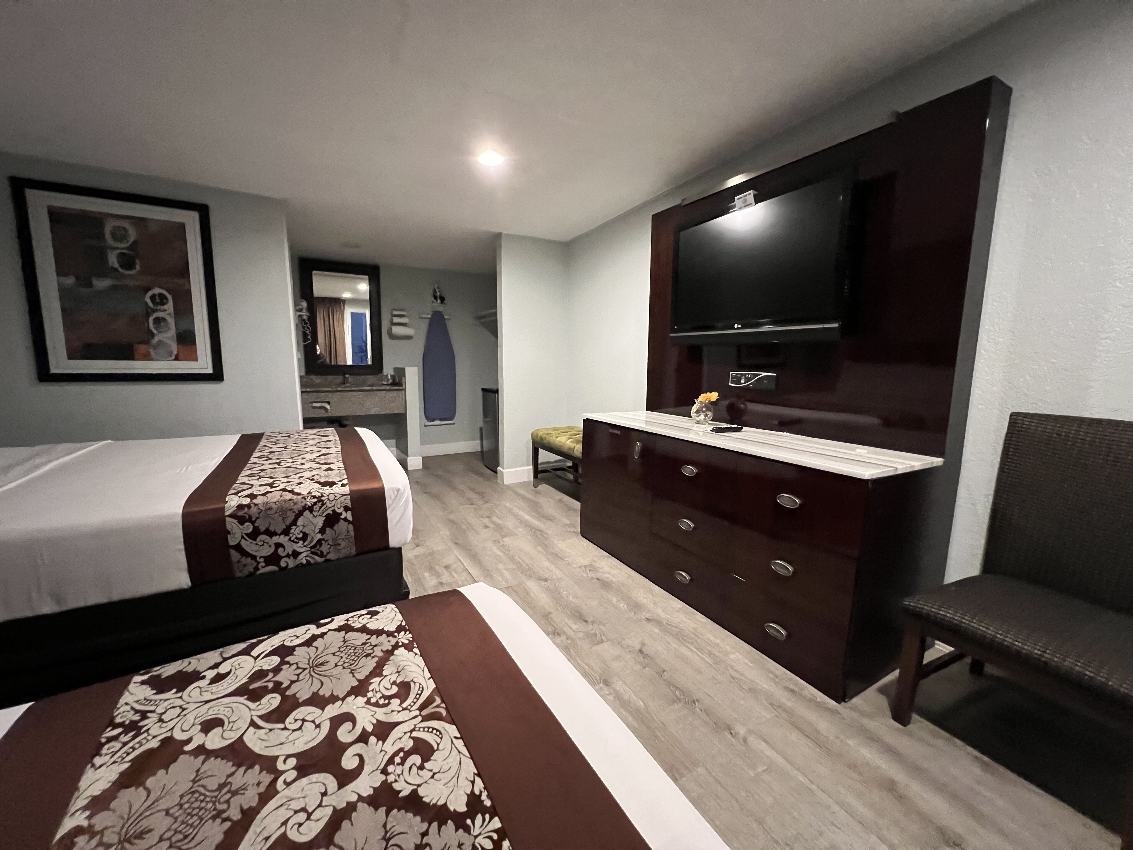 A hotel room with two beds, a dresser, a television, and a bathroom in the background.