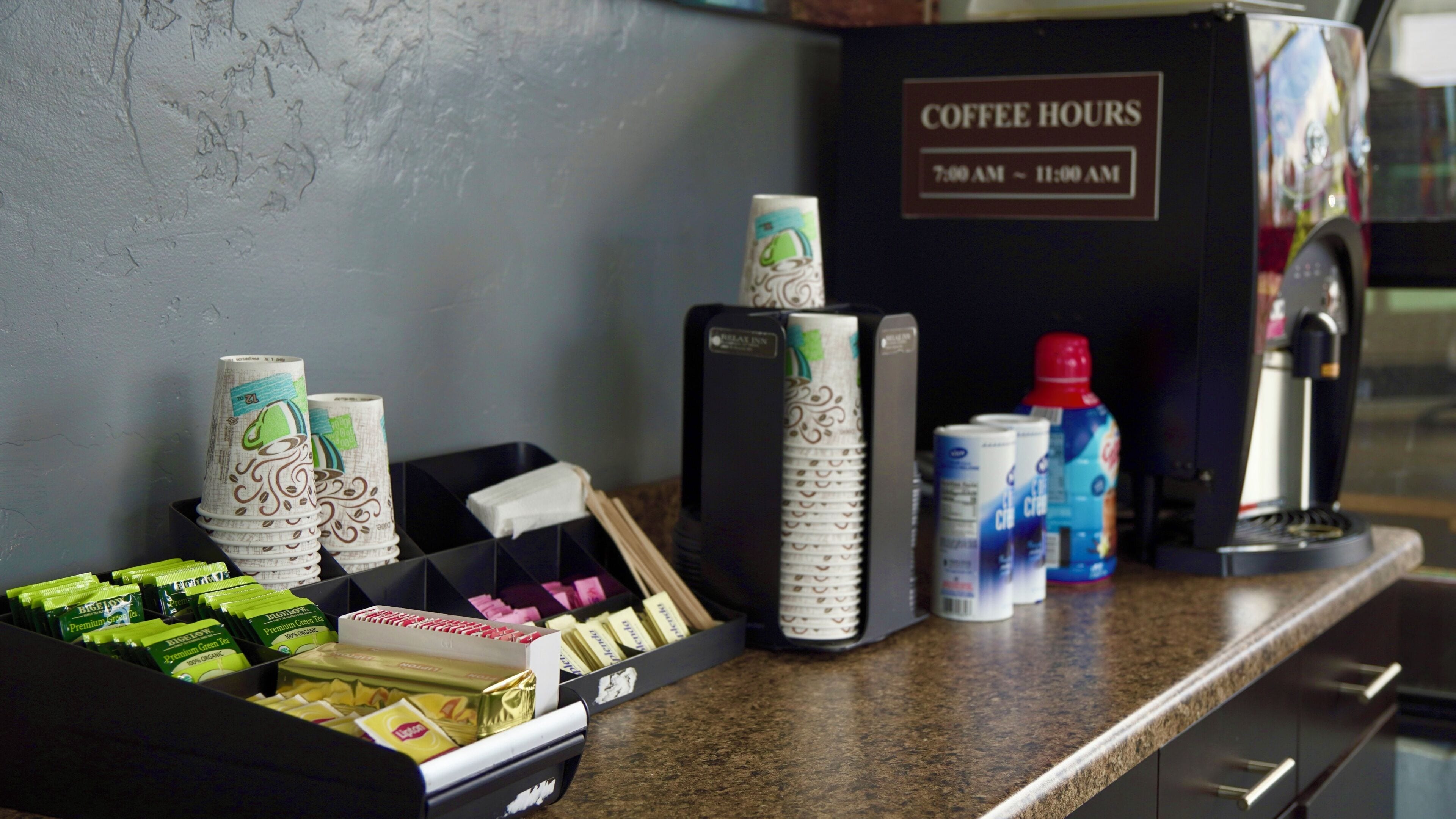 A coffee station with disposable cups, tea bags, and a coffee machine.