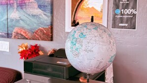 A room with a globe, a digital weather display, a framed painting, and a security camera.