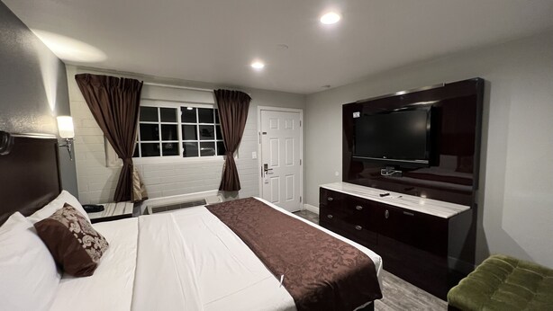 A hotel room with a bed, a dresser, a television, and a window with curtains. - Relax Inn Motel (Flagstaff)