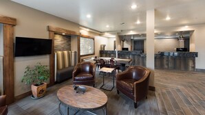 A spacious indoor area with leather chairs, a wooden table, a flat-screen TV, and a kitchen area in the background. - Third Street Inn (McCall)