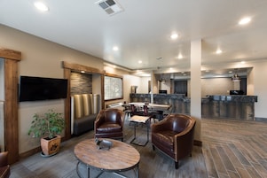 Un espacio interior amplio con sillones de cuero, una mesa de madera, un televisor de pantalla plana y una cocina al fondo.